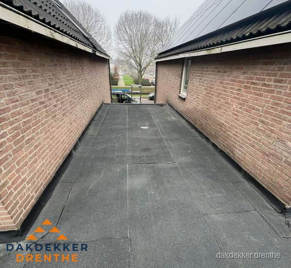 Plat dak met bitumen dakbedekking tussen bakstenen muren in Drenthe
